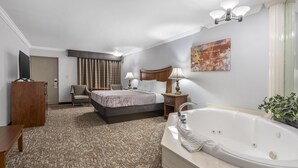 Une chambre d’hôtel avec un grand lit, un lit plus petit, un coin salon, un bureau, une télévision et une salle de bain avec baignoire, ainsi qu’un tableau accroché au mur.