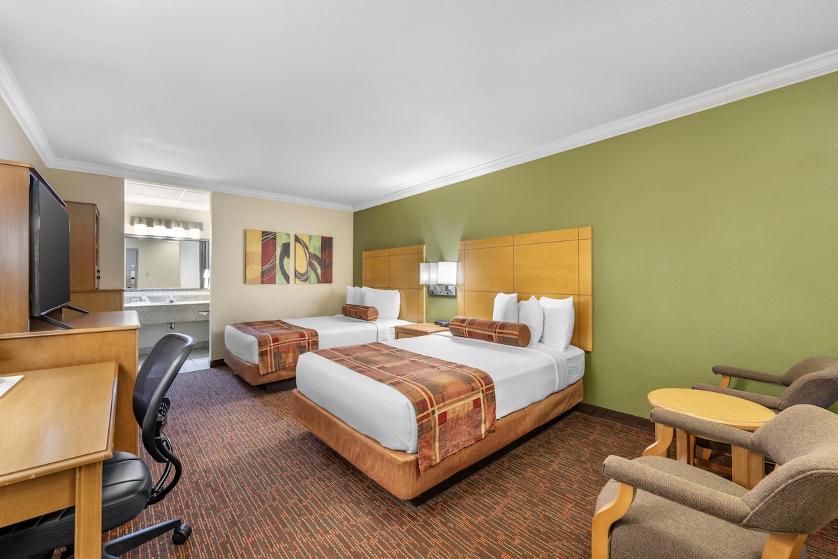 A hotel room with two beds, a desk, a chair, and a small table.