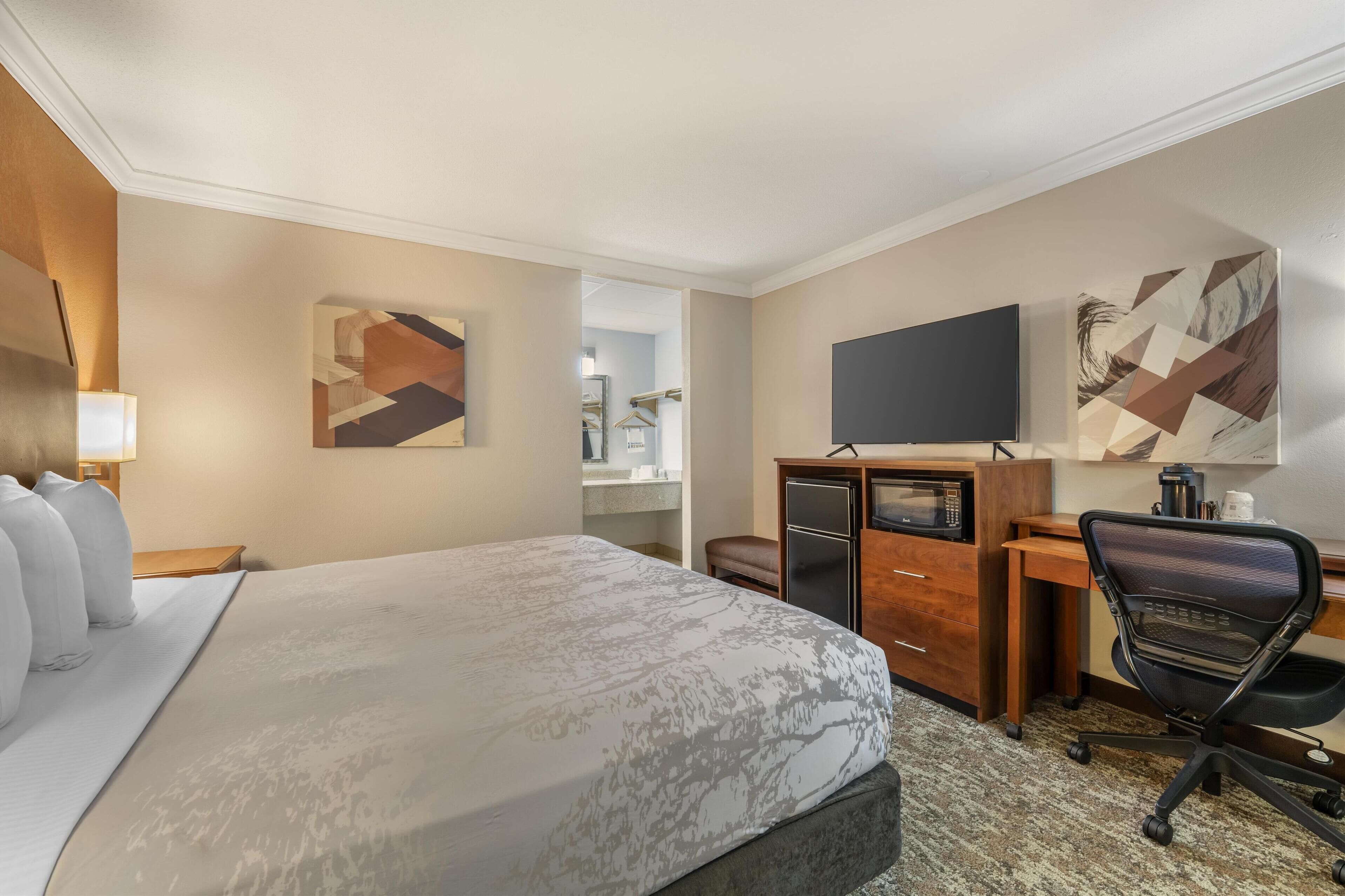 A hotel room with a large bed, a desk with a computer, a TV, and artwork on the walls.