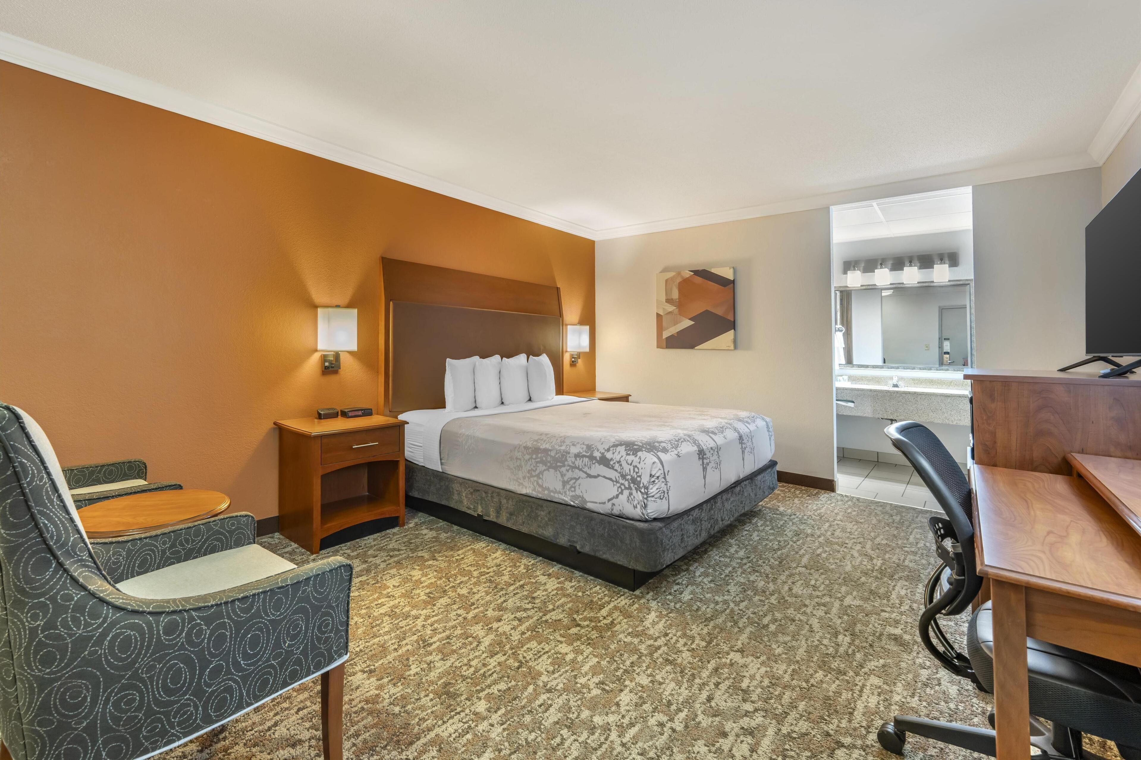 Habitación de hotel con cama, escritorio, silla, mesita de noche y un amplio ventanal.