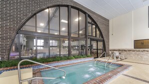 An indoor swimming pool with a brick border, large windows, and a view of the interior space. - Best Western Angus Inn (Great Bend)