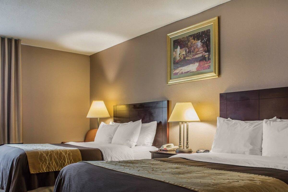A hotel room with two beds, each with a headboard, bedside lamps, and a painting on the wall.