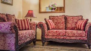 Une pièce comprenant deux canapés richement décorés, recouverts d’un tissu à motifs floraux, un plancher en bois, une lampe et un miroir encadré accroché au mur.