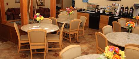 A hotel dining area with round tables, chairs, and flower arrangements.