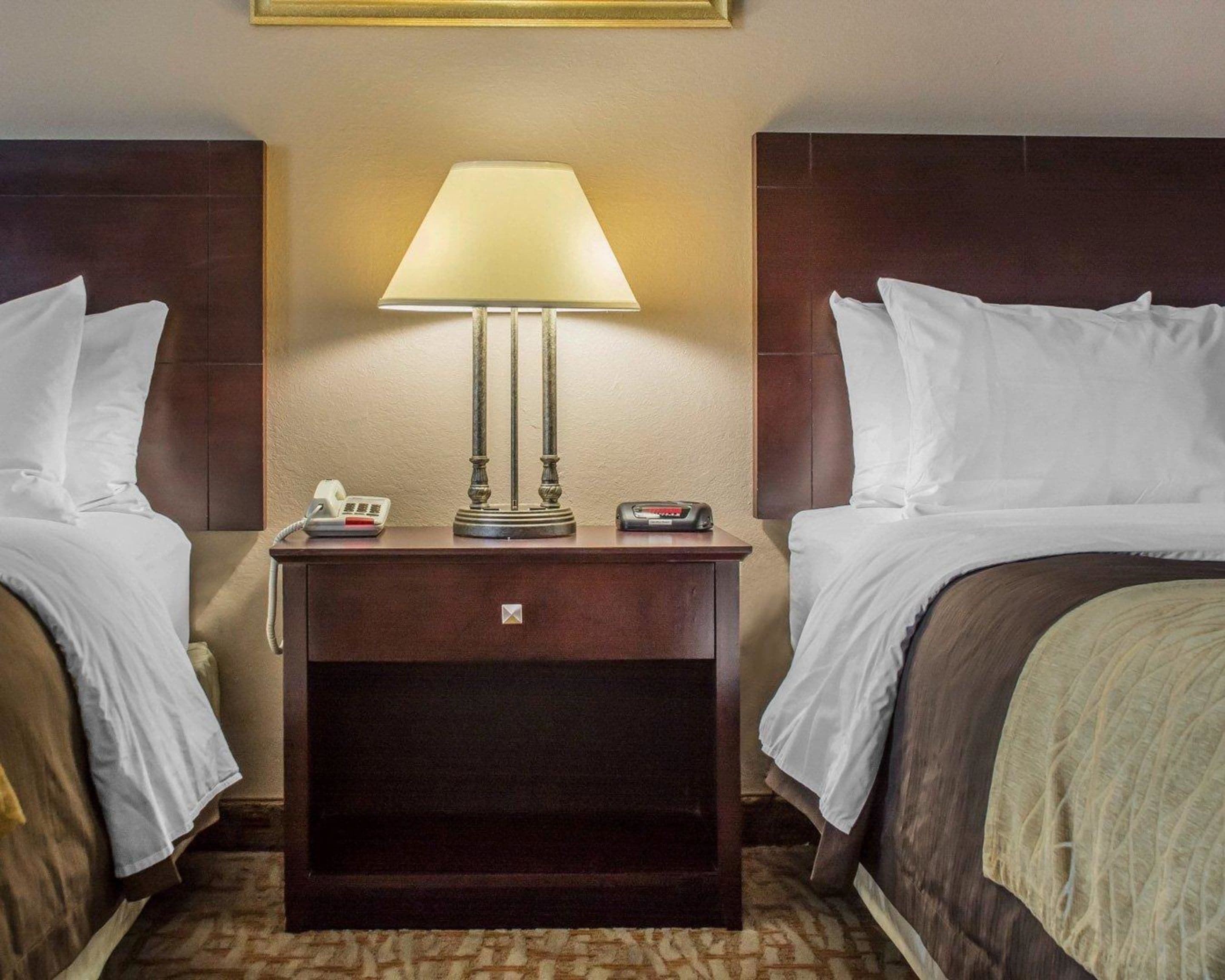 A hotel room with two beds, a nightstand with a lamp, a phone, and a clock.
