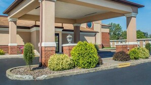Un bâtiment doté d’une entrée abritée, de colonnes en briques et d’un espace paysager agrémenté d’arbustes et d’un petit arbre.