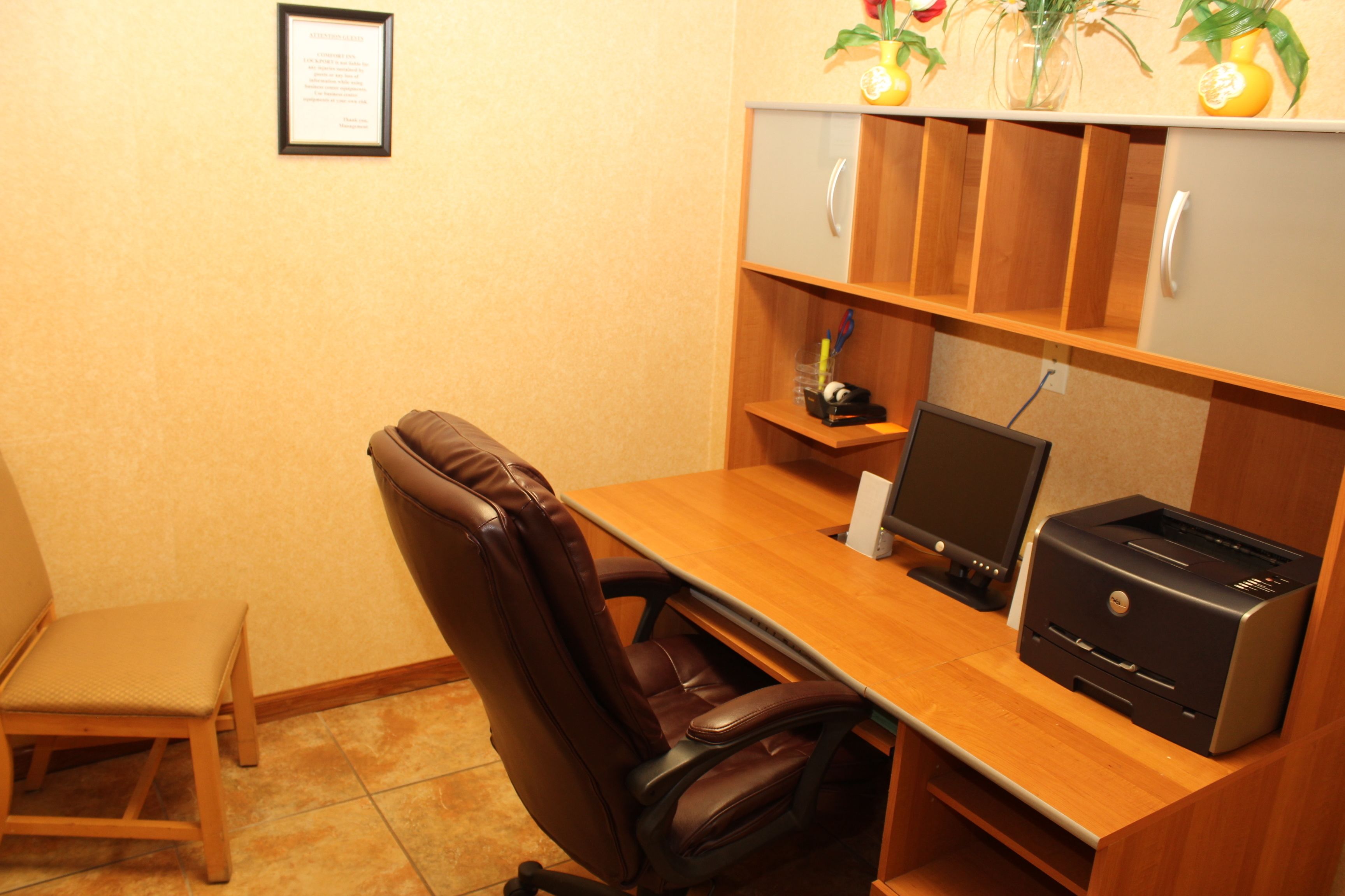 A small office with a desk, chair, printer, and a shelf with decorative items.