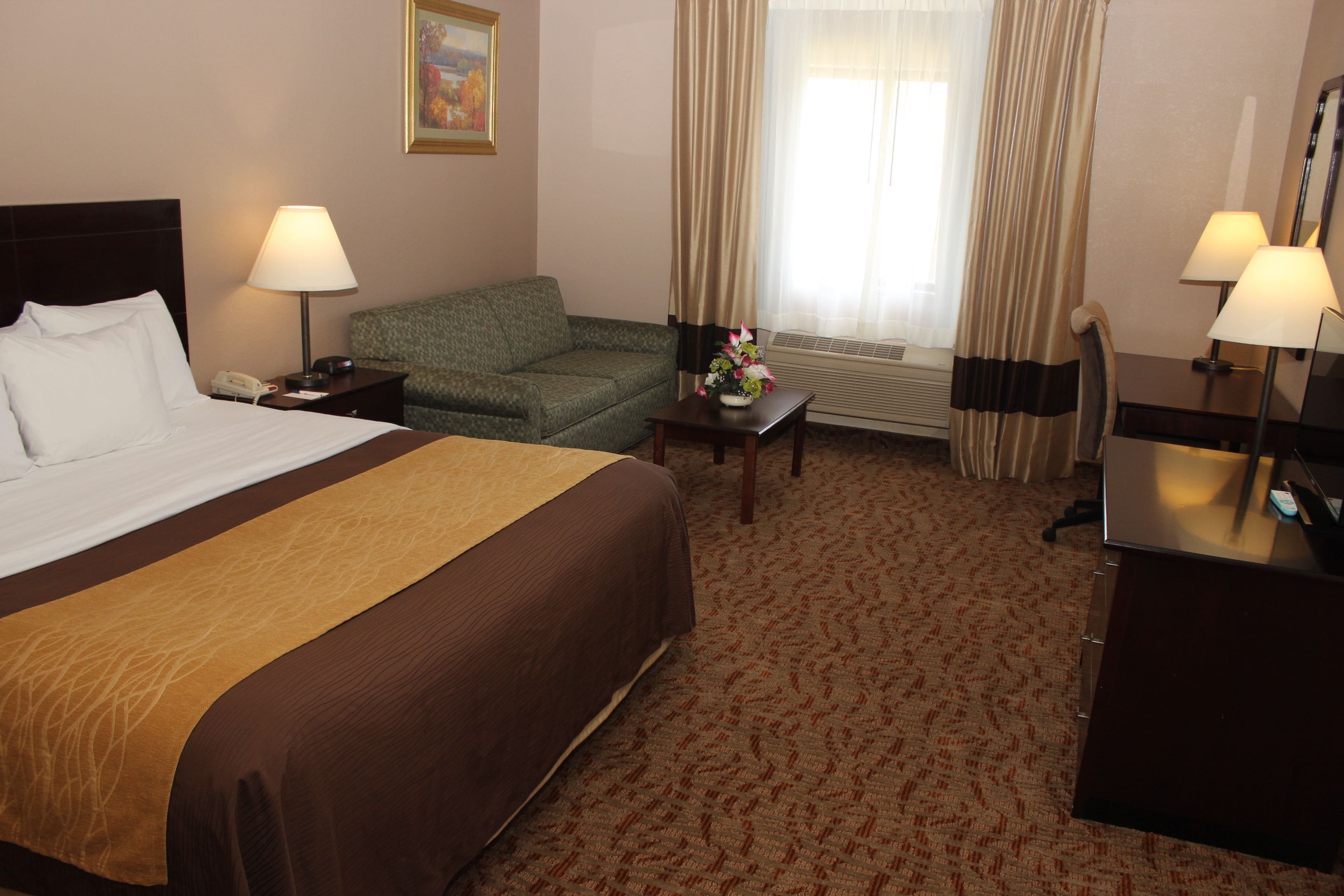 Ein Hotelzimmer mit einem großen Bett, einem grünen Sessel, einem kleinen Tisch mit einer Vase sowie einem Schreibtisch mit einer Lampe.