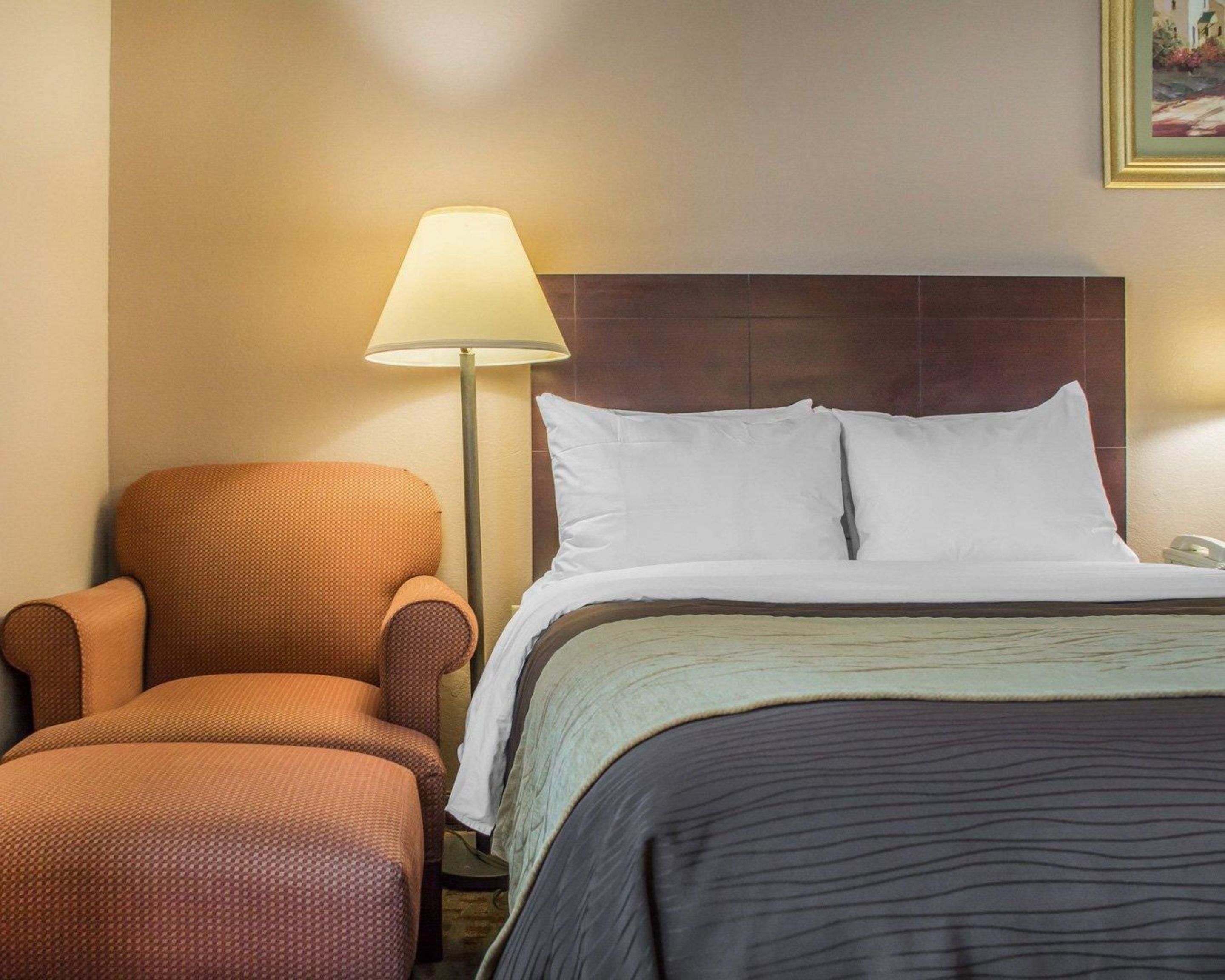 A hotel room with a bed, a chair, and a lamp.