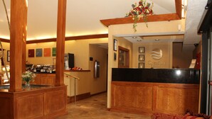 Un hall d’hôtel avec un comptoir d’accueil en bois, un coin cuisine et un espace détente avec un canapé à motifs.