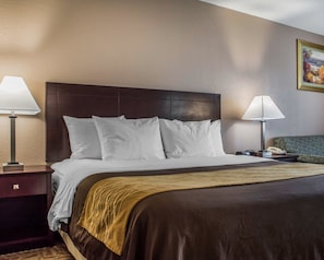 A hotel room with a large bed, two bedside lamps, a nightstand, a green upholstered chair, and a painting on the wall.