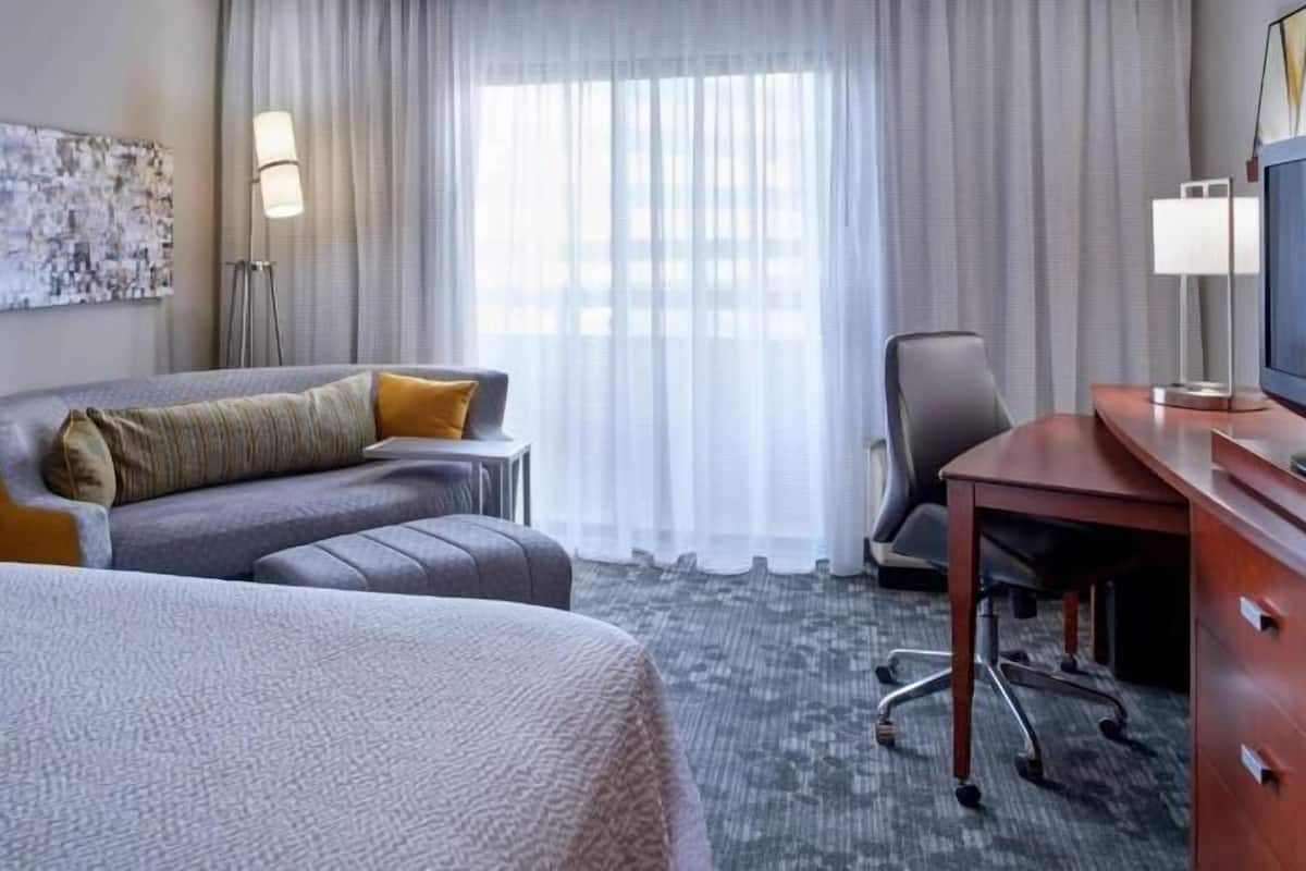 A hotel room with a bed, a sofa, a desk, a chair, and a large window with curtains.