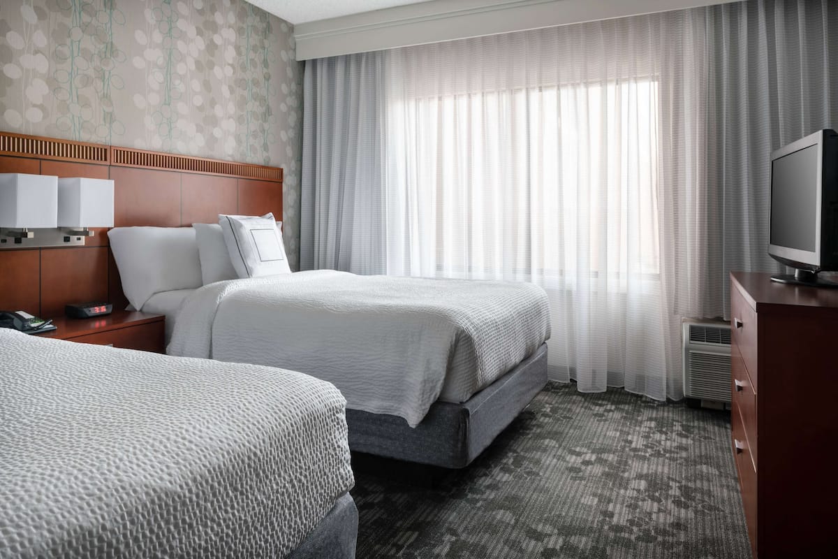 A hotel room with two beds, a TV, a bedside table with a phone, and a window with curtains.