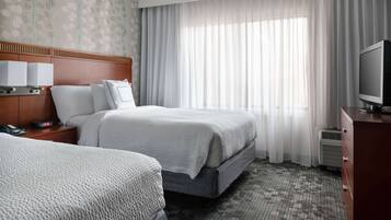 Habitación de hotel con dos camas, un televisor, una mesita de noche con teléfono y una ventana con cortinas.
