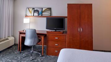 Una camera d'albergo con un letto, una scrivania con un monitor del computer, una sedia, un armadio e un termosifone.