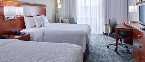 Une chambre d’hôtel avec deux lits, un bureau, une chaise, une télévision et une lampe.