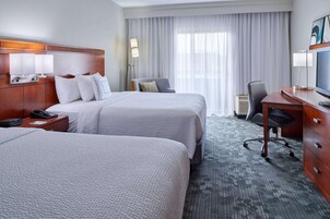 Habitación de hotel con dos camas, un escritorio, una silla, un televisor y una lámpara.