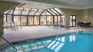Una piscina interior con paredes de vidrio transparente, sillas de descanso y suelo de baldosas.