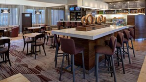 Un moderno vestíbulo de hotel con una zona de bar, diferentes disposiciones de asientos y una pantalla grande mostrando contenido.