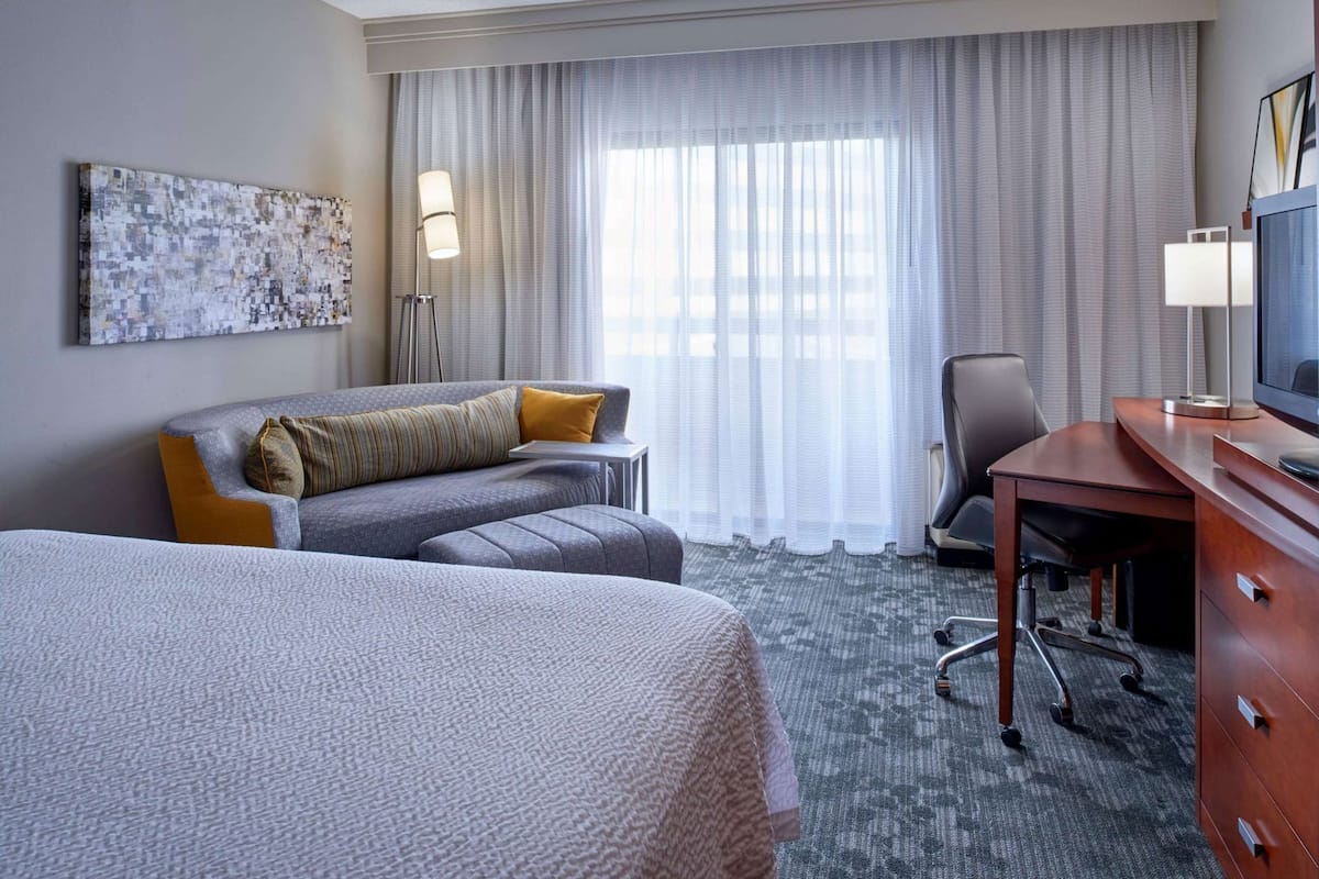 A hotel room with a large bed, a sofa, a desk, and a television.