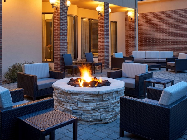 An outdoor patio with stone fire pit, wicker furniture, and brick walls.