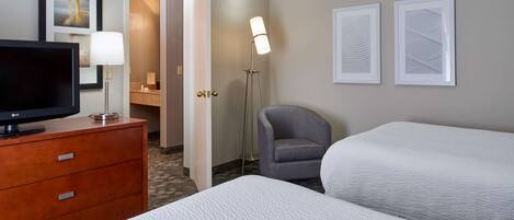 A hotel room with two beds, a TV on a wooden dresser, a lamp, and framed artwork on the wall.