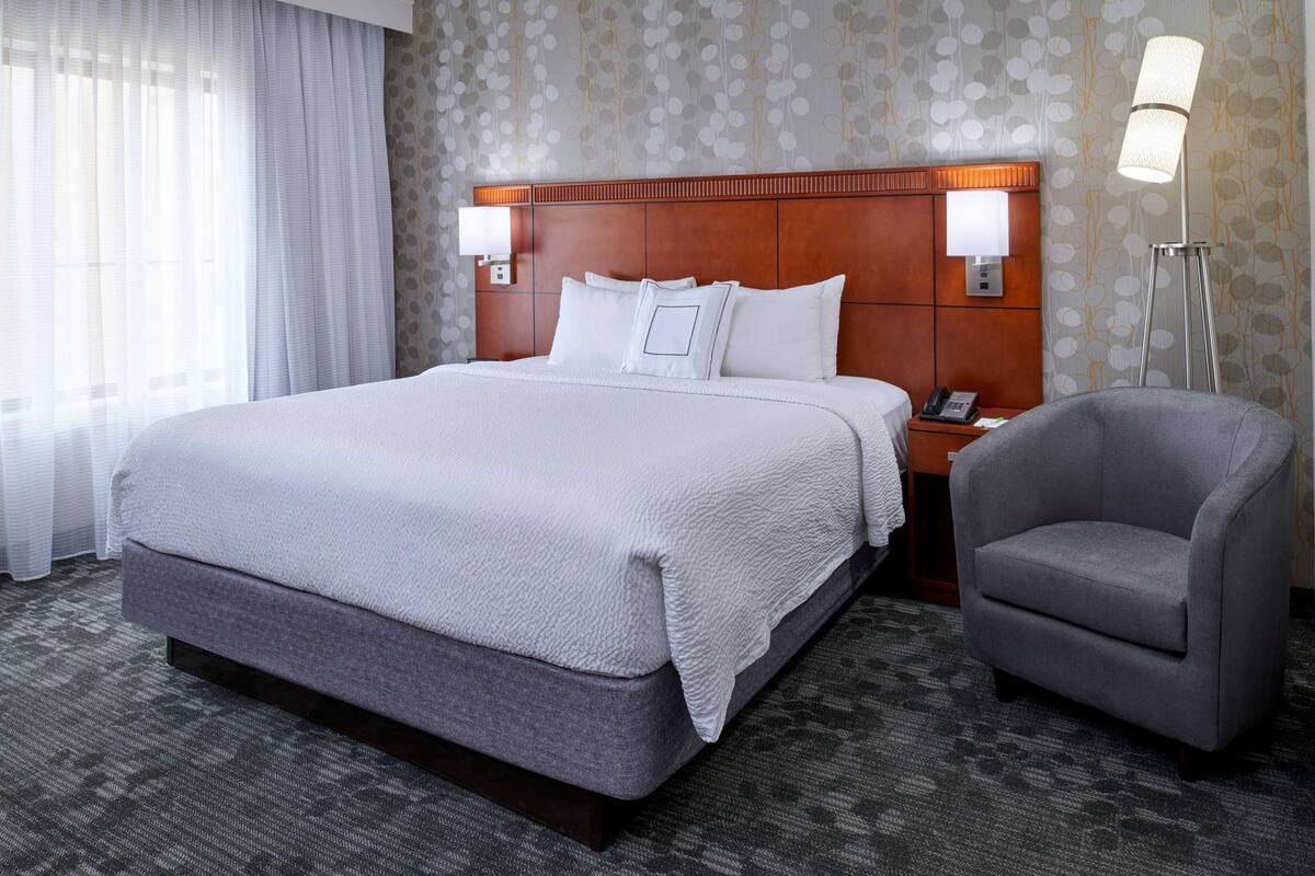 A hotel room with a large bed, two bedside lamps, a chair, and a nightstand with a phone.