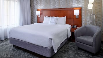 A hotel room with a large bed, two bedside lamps, a chair, and a nightstand with a phone.