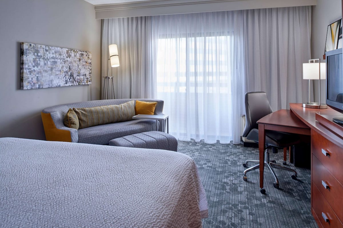 A hotel room with a bed, a sofa, a desk, a chair, and a television.