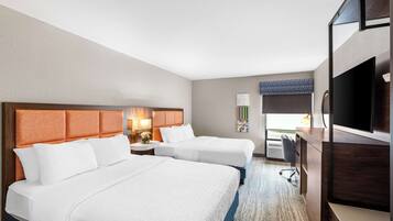 A hotel room with two beds, a desk, a TV, and a window with a view.
