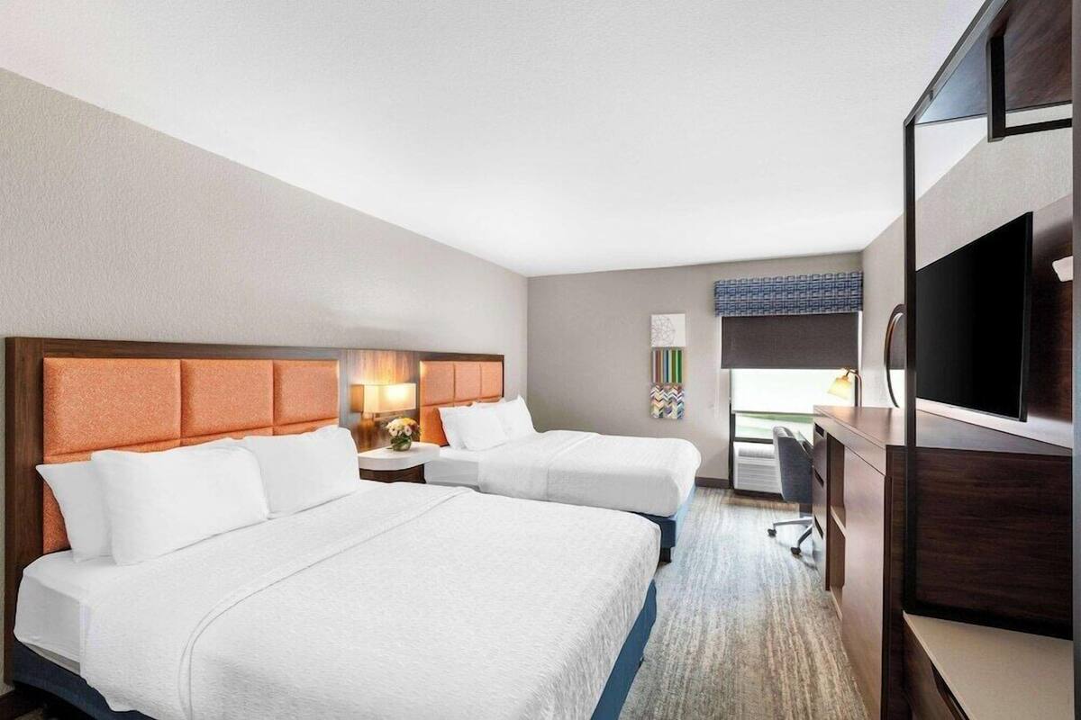 Habitació d'hotel amb dos llits, un escriptori, una televisió i una finestra.