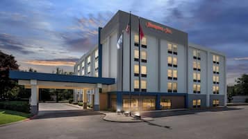 A Hampton Inn hotel with a clear entrance, a covered parking area, and a flagpole with flags.