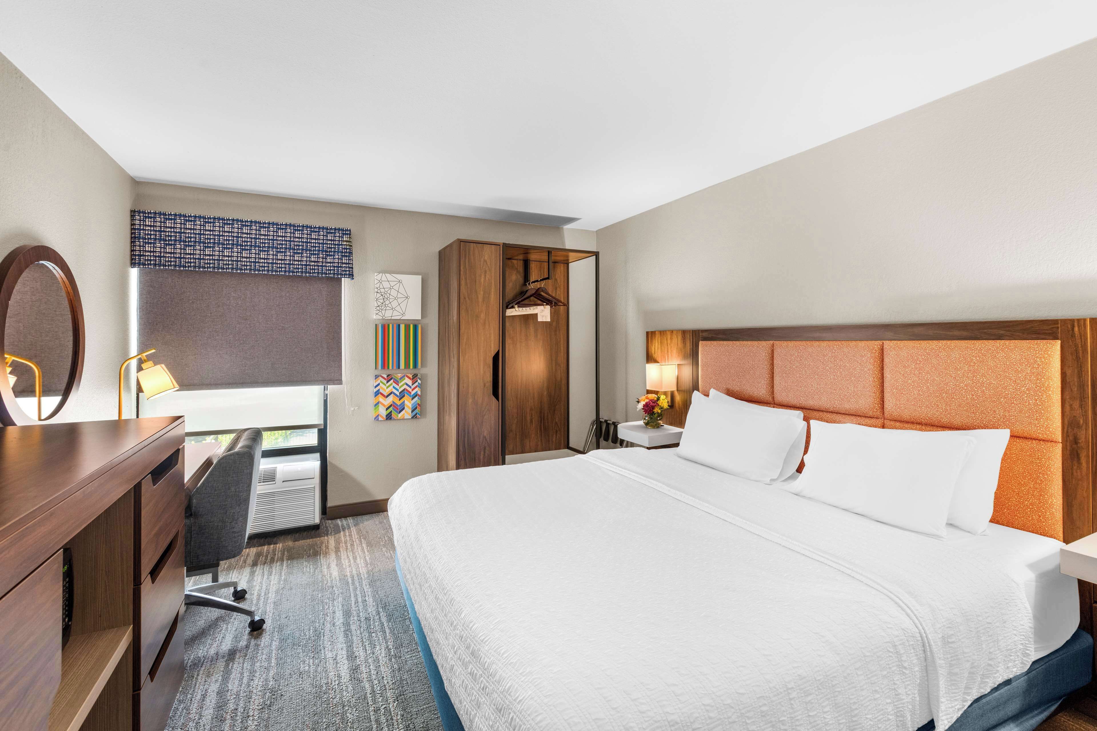 A hotel room with a large bed, a desk with a chair, a wardrobe, and a mirror.