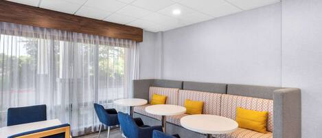 Una habitación de hotel moderna con un sofá gris, sillas azules y mesitas redondas pequeñas.