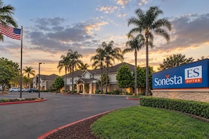 Entrada a un hotel Sonesta Suites, con cielo despejado y palmeras.