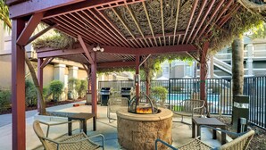 An outdoor patio with a fire pit, wicker furniture, and a pool in the background. - Sonesta ES Suites San Jose Airport (San Jose)