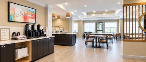 Una cucina moderna con un angolo caffè, un'area pranzo con tavoli e sedie, e una scala con ringhiera in legno.