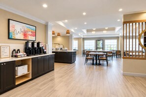 Une cuisine moderne dotée d’un coin café, d’un espace repas avec tables et chaises, et d’un escalier avec une rampe en bois.