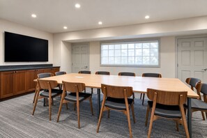 Un salón de conferencias con una mesa grande, sillas, un televisor de pantalla plana y un ventanal.