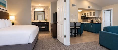 A hotel room with a bed, a desk, a kitchenette, and a bathroom.