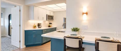 Una cocina moderna con una isla central, armarios blancos y microondas integrado.