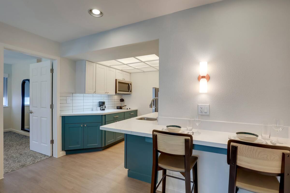 Una cocina moderna con armarios color turquesa, encimera blanca y una isla central con dos taburetes de bar.