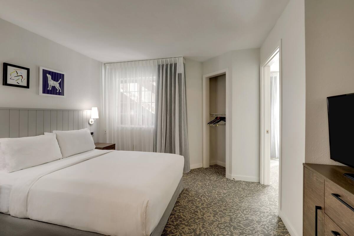 Habitación de hotel con una cama grande, televisión, armario y puerta que da a un pasillo.