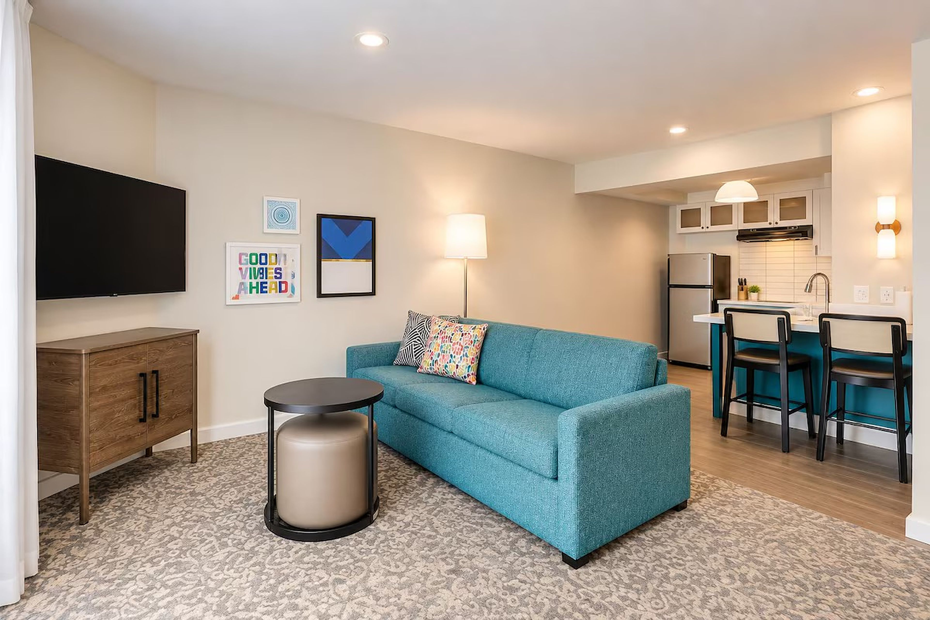 A compact living space with a sofa, a small round table, a cabinet, a television, and a kitchenette area.