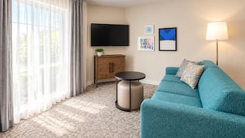 Una sala moderna con un sofá azul turquesa, un televisor de pantalla plana, un mueble aparador, una mesita redonda y una lámpara.