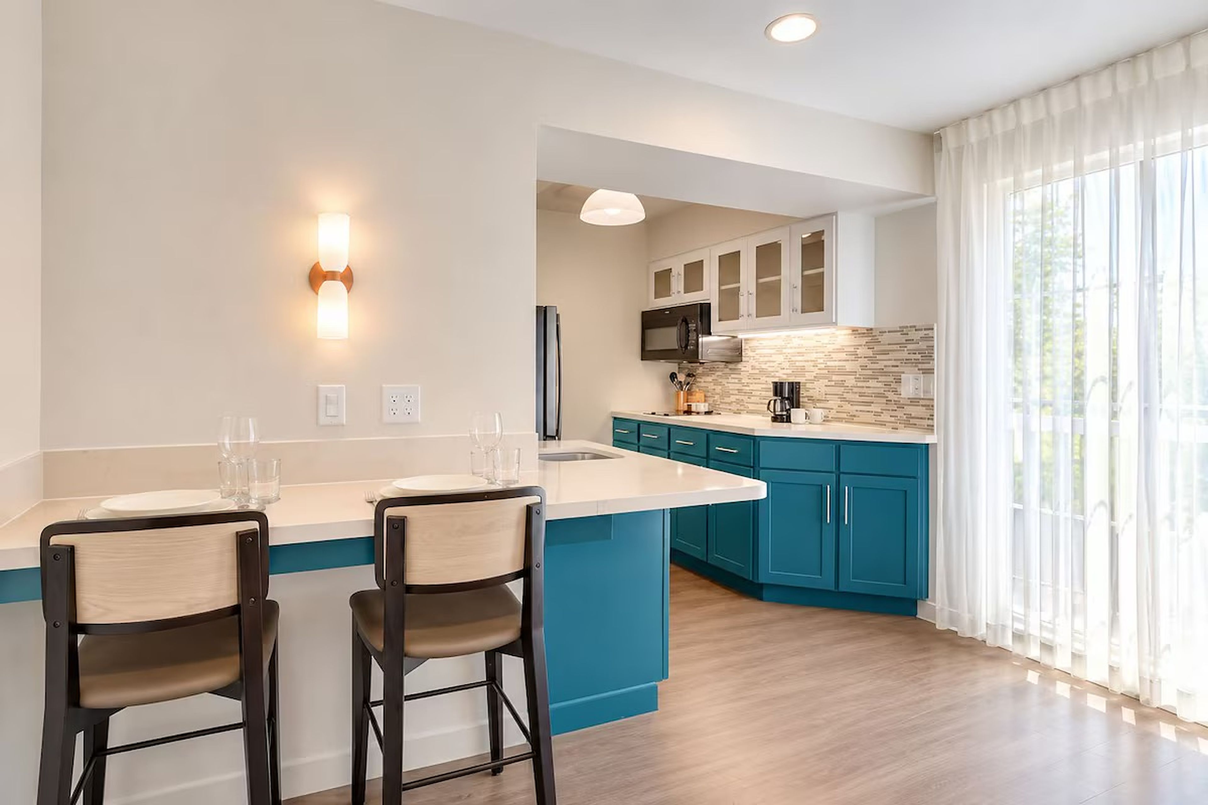 A modern kitchen with a central island, bar stools, and a view of the outdoors.