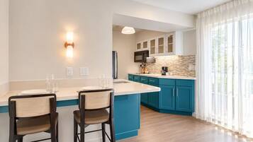A modern kitchen with a central island, bar stools, and a view of the outdoors.