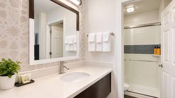 A modern bathroom with a large mirror, a sink, a potted plant, and a shower area.