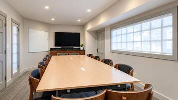 A conference room with a long table, chairs, a flat-screen TV, and windows.