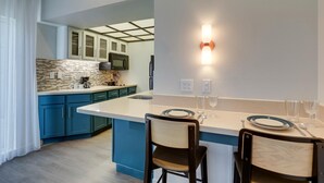 A modern kitchen with teal cabinetry, a white countertop, and a central island. There are two chairs and a dining table set up for a meal. - Sonesta ES Suites San Jose Airport (San Jose)